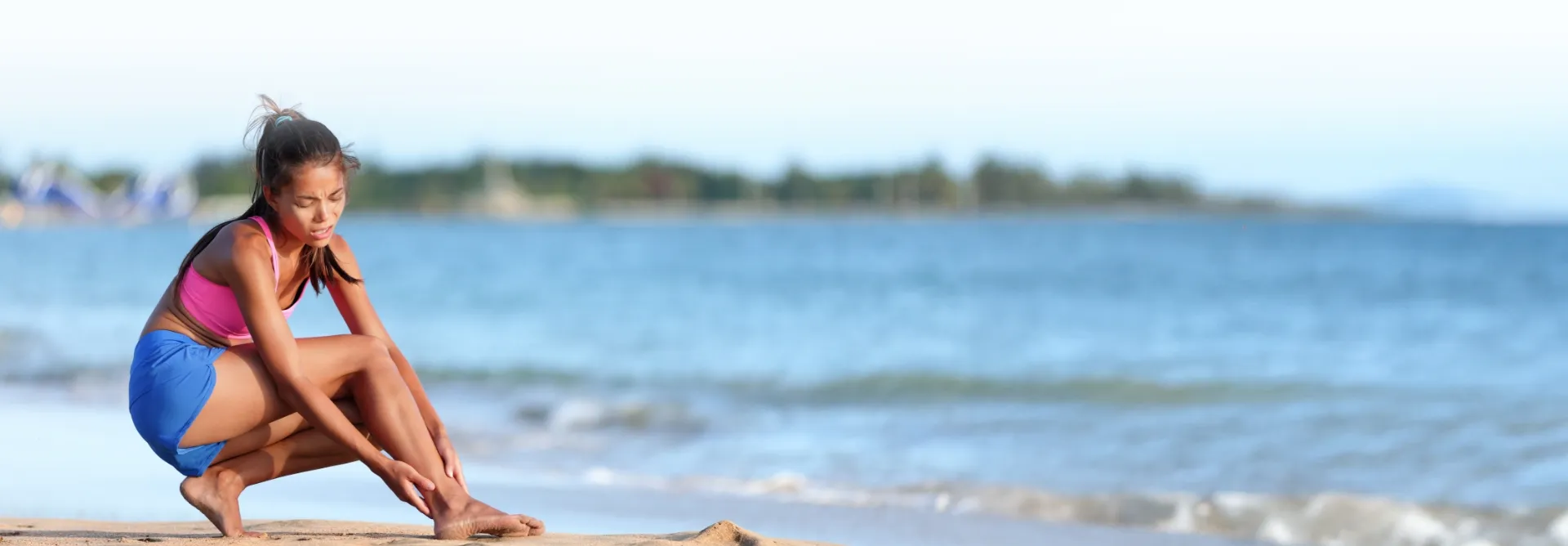 woman holding injured ankle on the beach